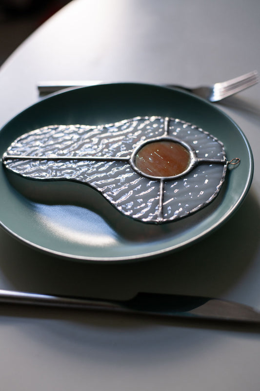 Teal plate with a decorative egg-shaped stained glass artwork, fork, knife, and glass on a white surface.