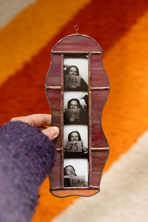 Colorful stained glass frame with photobooth photos inside, held by a hand against an orange background
