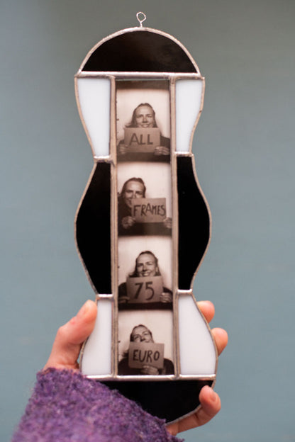 Black and white stained glass frame with photobooth photos inside, held by a hand against a blue background