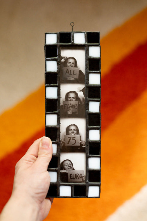 Hand holding a black and white photo frame with cut-out images inside.