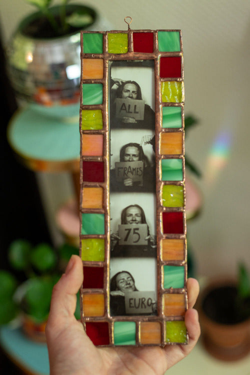 Colorful stained glass frame with photobooth photos inside, held by a hand.