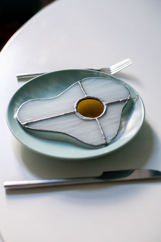 Teal plate with a decorative egg-shaped stained glass artwork, fork, knife, and glass on a white surface.