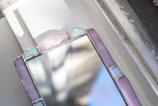 Stained glass mirror panel with a geometric design featuring pink and white colors.