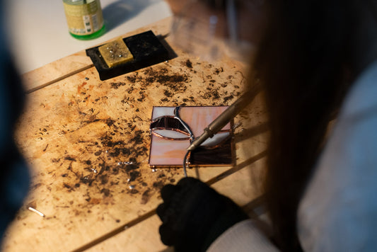 Someone soldering a stained glass art work with a solder iron on a wooden plate