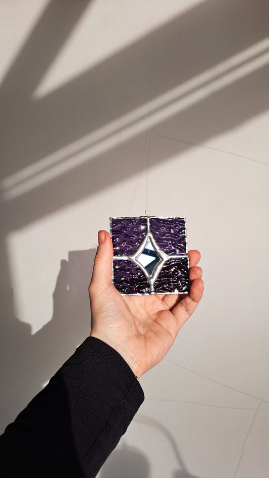 Hand holding a small square tile with a star design against a light background