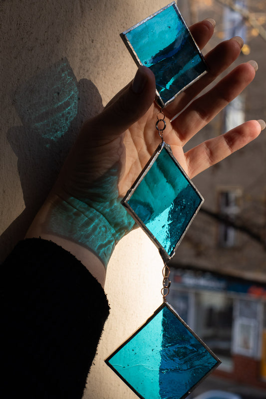 Turquoise glass suncatcher held in a hand against a blurred background