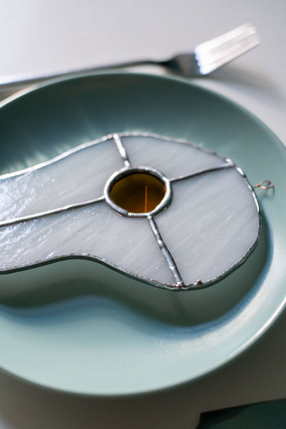 Teal plate with a decorative egg-shaped stained glass artwork, fork, knife, and glass on a white surface.
