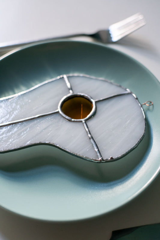 Teal plate with a decorative egg-shaped stained glass artwork, fork, knife, and glass on a white surface.