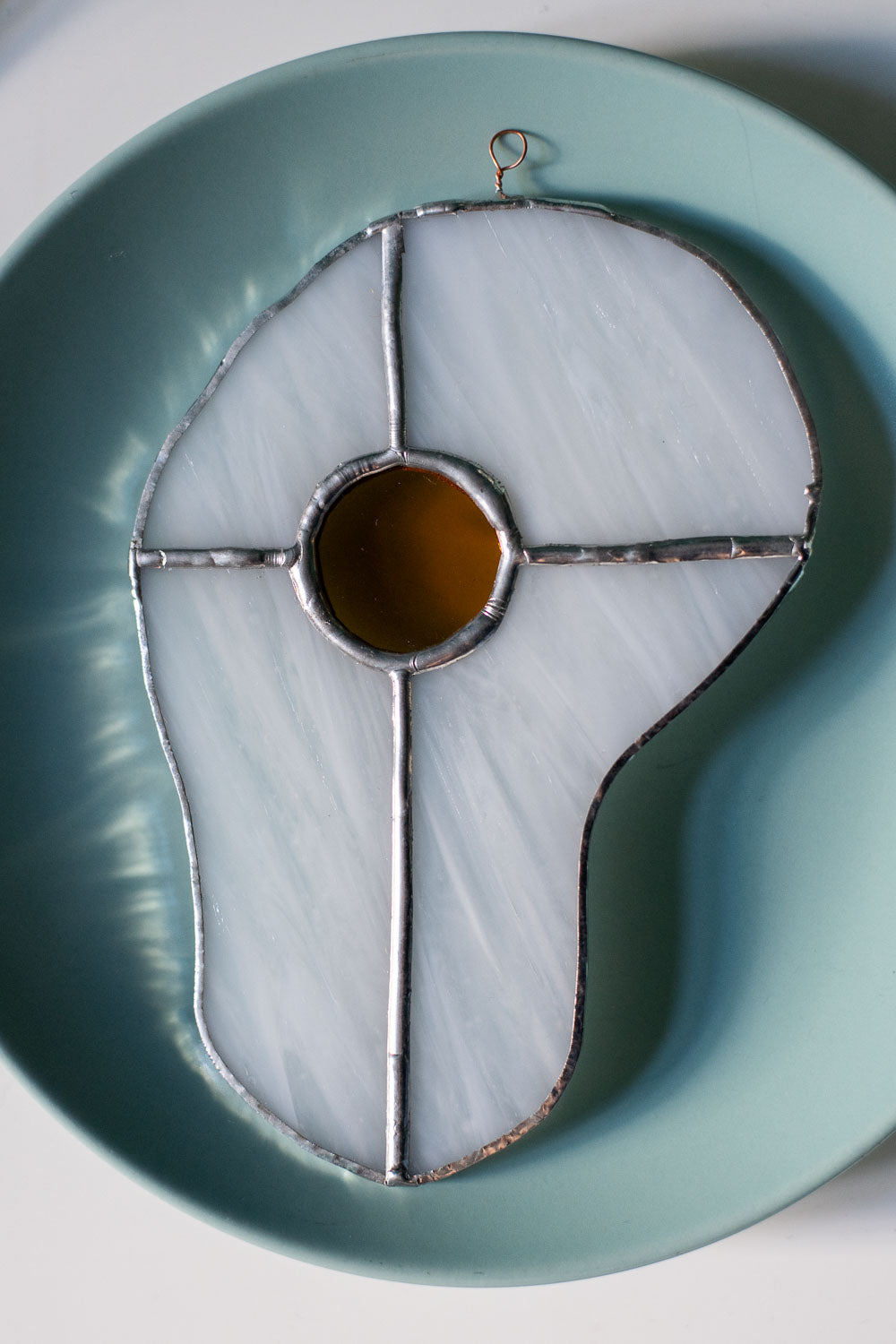 Teal plate with a decorative egg-shaped stained glass artwork, fork, knife, and glass on a white surface.