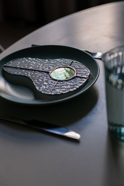 Teal plate with a decorative egg-shaped stained glass artwork, fork, knife, and glass on a white surface.