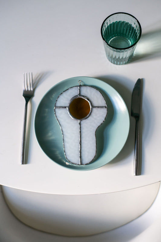 Teal plate with a decorative egg-shaped stained glass artwork, fork, knife, and glass on a white surface.