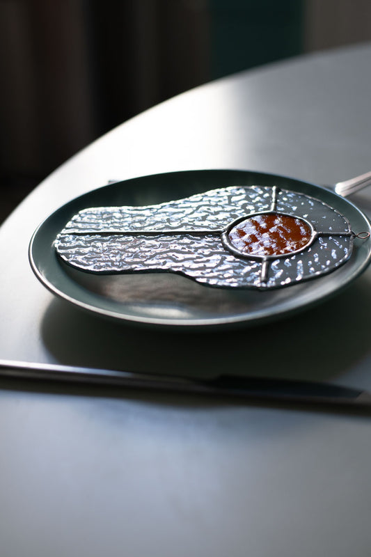 Teal plate with a decorative egg-shaped stained glass artwork, fork, knife, and glass on a white surface.