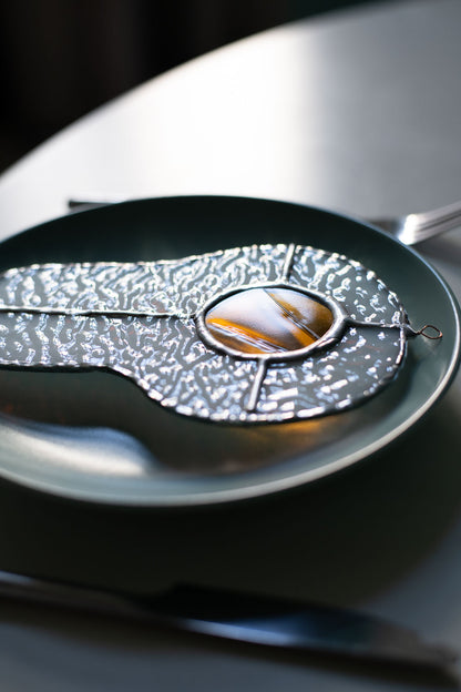 Teal plate with a decorative egg-shaped stained glass artwork, fork, knife, and glass on a white surface.