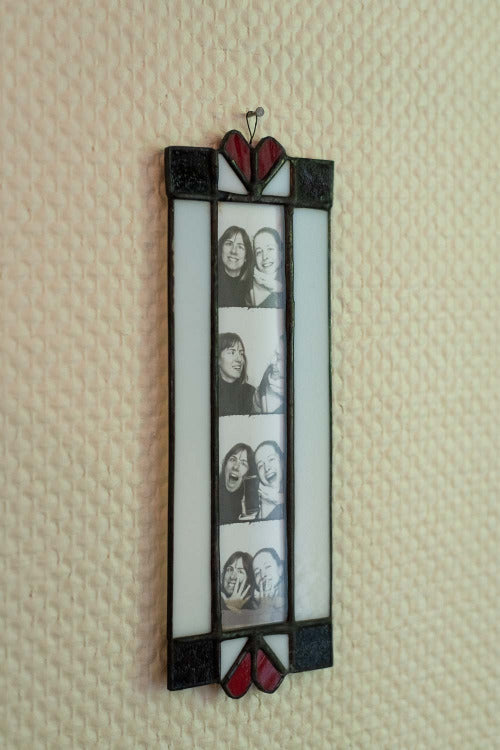Stained glass photo frame with heart designs on a textured wall