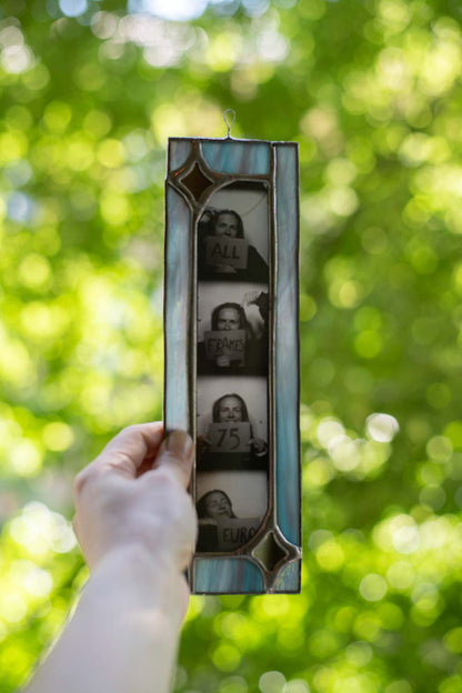 Person holding a vintage-style photo frame with portraits against a blurred green outdoor background