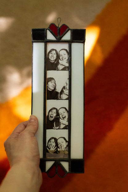 Stained glass panel with photo booth images held by a hand against a warm-toned background
