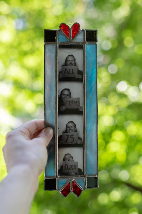 Stained glass picture frame held against a blurred green outdoor background.