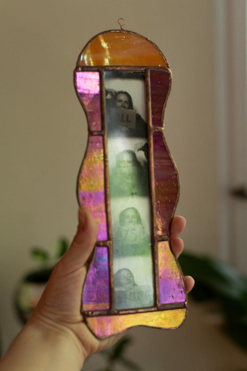 Colorful stained glass frame with photobooth photos inside, held by a hand.