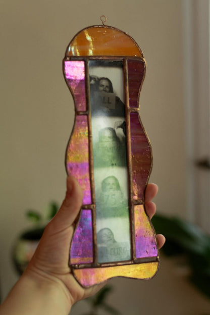Colorful stained glass frame with photobooth photos inside, held by a hand.