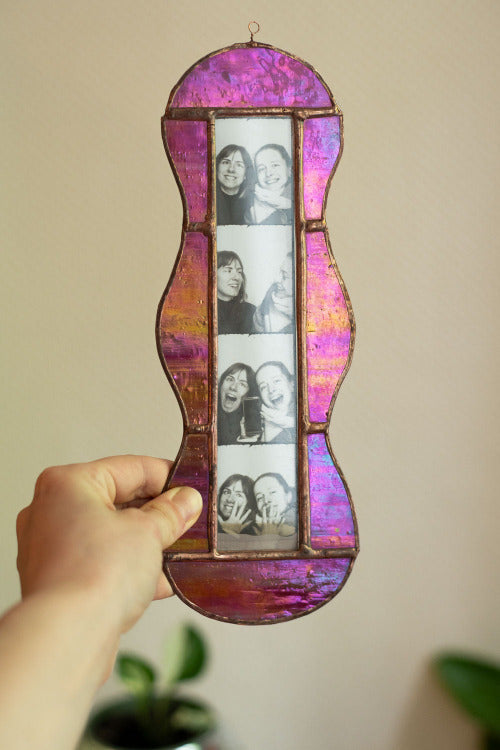 Colorful stained glass frame with photobooth photos inside, held by a hand against a beige background