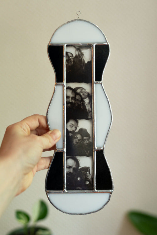 Black and white stained glass frame with photobooth photos inside, held by a hand against a beige background