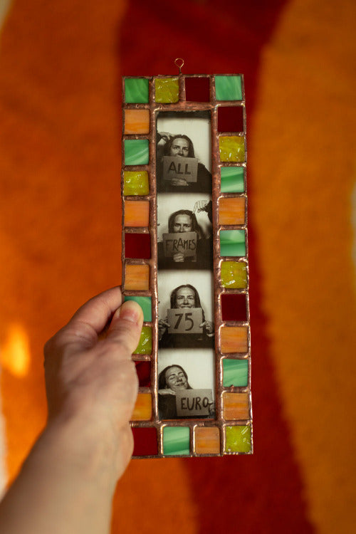 Colorful stained glass frame with photobooth photos inside, held by a hand in front of an orange background