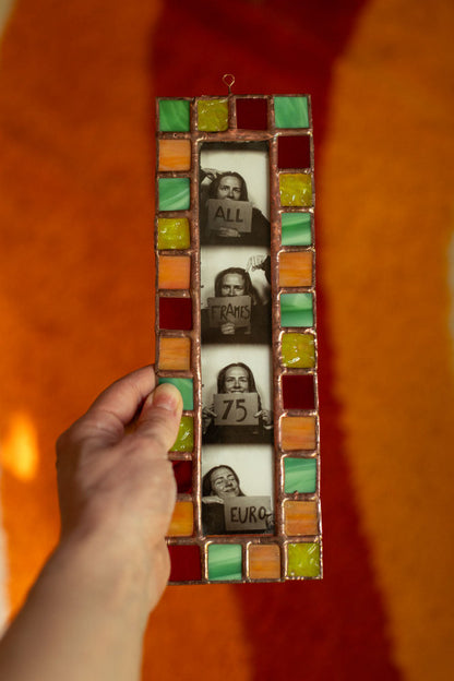 Colorful stained glass frame with photobooth photos inside, held by a hand in front of an orange background